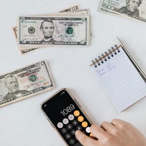 Overhead view of a hand using a calculator with US dollars and notes, representing finance and budgeting.